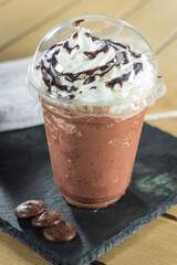Chocolate smoothie with whipped cream in plastic cup on wooden table