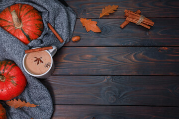 Cup of spicy autumn latte coffee at warm comfortable plaid, scarf, thanksgiving orange pumpkins, spices on dark brown wooden table. Top view with rustic background and copy space
