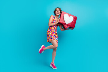 Full length photo of dreamy funky girl dressed print outfit holding feedback heart looking empty space isolated blue color background