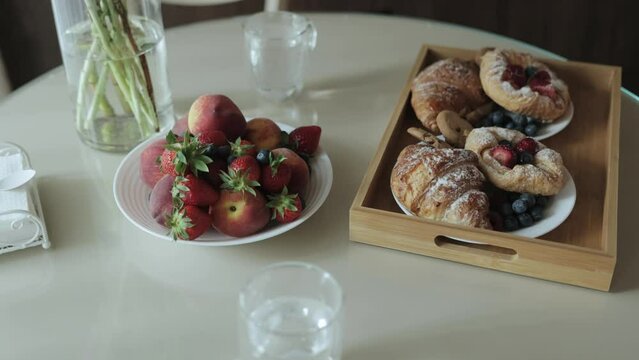 Close-up of breakfast. Kitchen with delicious breakfast buns and croissant with jam beautifully served on wooden tray plat, fruits on the background. Breakfast at home, no people, slow motion.