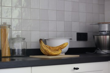 A portrait of a bunch of yellow bananas lying on a white plastic cutting board on a black kitchen countertop. The delicious energizing food is ready to eat and ideal before sport.