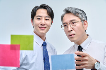 Two businessmen are standing on the glass wall of the office, looking at the attached paper and...