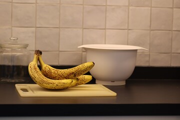 A portrait of a bunch of yellow bananas lying on a white plastic cutting board on a black kitchen...