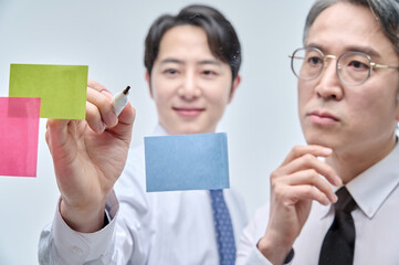 Two businessmen are standing on the glass wall of the office, looking at the attached paper and contemplating planning and strategy.