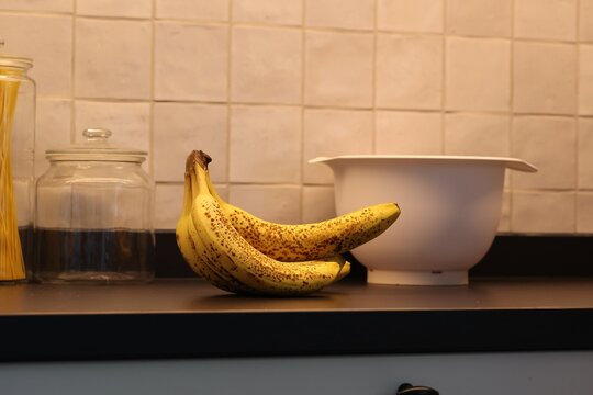 A portrait of a bunch of yellow bananas with som brown spots lying on a black kitchen countertop. The delicious energizing food is ready to eat and ideal before a sport activity.