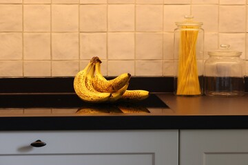 A portrait of a bunch of yellow bananas with some brown spots on a induction stove or cooker in a...