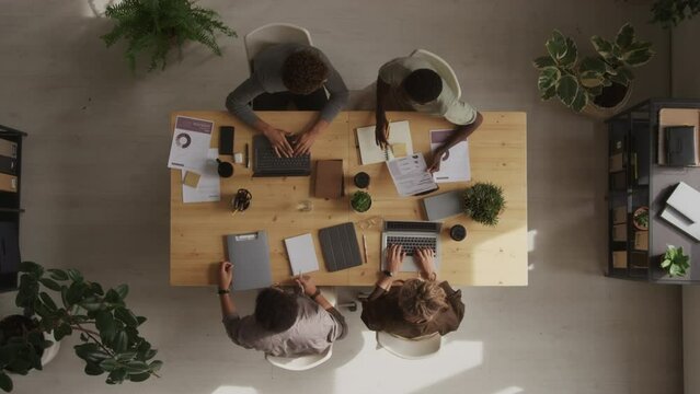 Top view stab shot of two diverse business couples having negotiations at wooden desk in modern office, discussing contract and shaking hands in agreement