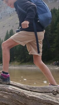 A young adventurer strolls along a fallen tree by a mountain lake in a U.S. national park. Focus on legs and boots, showcasing a childhood immersed in nature. The vertical video captures the essence