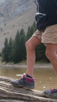 A boy walks on a fallen tree trunk near a mountain lake in a U.S. national park. Detail of legs and boots Adventure, growth, childhood nature connection, environmental education. Overcoming challenge

