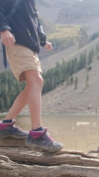 A youngster explores the wild, navigating a fallen tree by a mountain lake in a U.S. national park. Zooming in on legs and boots, it encapsulates a childhood immersed in nature, fostering growth 