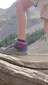 A boy walks on a fallen tree trunk near a mountain lake in a U.S. national park. Detail of legs and boots Adventure, growth, childhood nature connection, environmental education. Overcoming challenge
