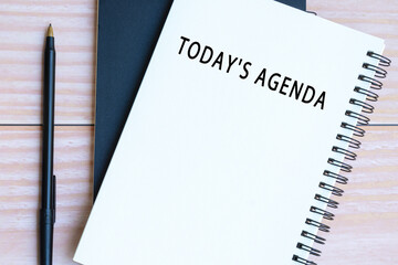 Today's agenda text on notepad with pen on wooden desk.