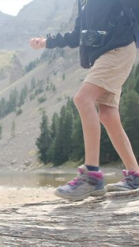 A boy walks on a fallen tree trunk near a mountain lake in a U.S. national park. Detail of legs and boots Adventure, growth, childhood nature connection, environmental education. Overcoming challenge

