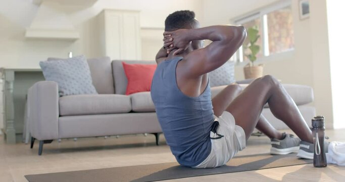 Focused african american man doing crunches in sunny living room, slow motion