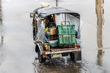 Taxi motor tricycle, tuk tuk, loaded with cargo is drives on the street in the rain, Bangkok,...