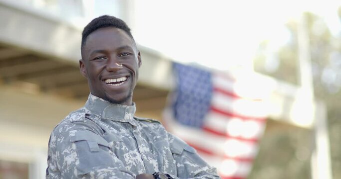 Happy african american male soldier laughing with flag in background on sunny day, slow motion
