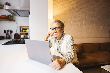 Senior smiling woman sufing the net with a laptop in living room at home.