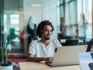 An African-American male, utilizing adaptive technology in his wheelchair, seamlessly integrates into a modern office space, embodying inclusivity and independence as he engages with a laptop