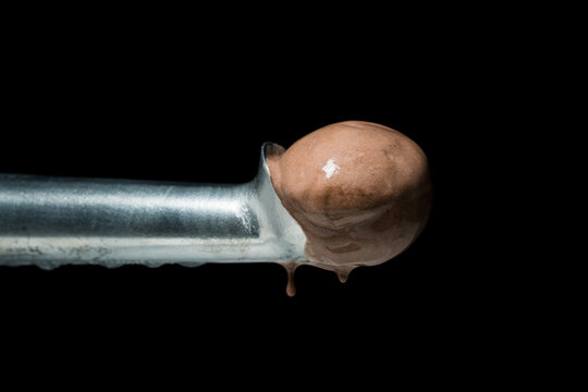 A metal spoon with a melting chocolate ice cream scoop dripping drops from it. Isolated on a black background.