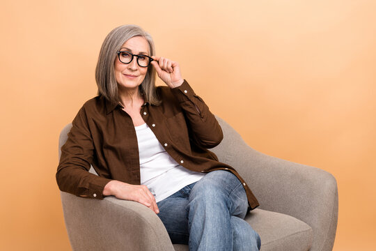 Portrait photo of confident businesswoman elderly touch eyeglasses sit chair boss waiting coffee isolated on beige color background