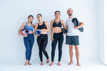 Fototapeta premium Group of three female friends and a man wearing exercise clothes holding yoga mats preparing to do yoga exercises together in studio.Healthy lifestyle concept