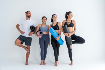 Fototapeta na wymiar Group of three female friends and a man wearing exercise clothes holding yoga mats preparing to do yoga exercises together in studio.Healthy lifestyle concept
