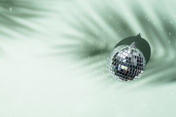 Shining disco ball on green background with palm leaves shadows