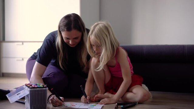 Little girl with her mother is painting on the floor at home