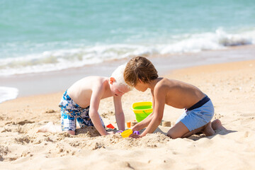 Children two little boys playing on the beach on summer holidays. Children having fun with a sand on the seashore. Vacation concept. Happy sunny day. Joyful children with beautiful sea, sand