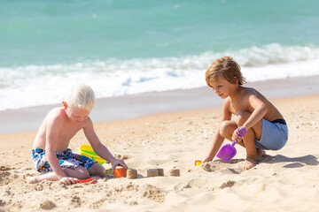 Naklejka premium Children two little boys playing on the beach on summer holidays. Children having fun with a sand on the seashore. Vacation concept. Happy sunny day. Joyful children with beautiful sea, sand
