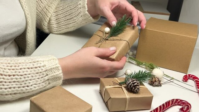 a woman decorates a box wrapped in crab paper with a fir branch and shows it to the camera, Christmas gifts