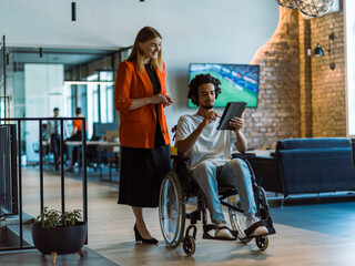 African-American businessman in a wheelchair engages in a collaborative discussion, using a tablet,...