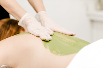 Woman receiving a therapeutic back massage with green algae, emphasizing relaxation and natural skincare treatment