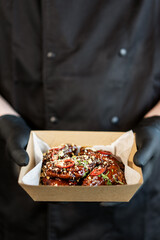The cook holds in his hands a box with grilled spicy chicken