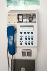 Old public telephone for making voice calls using coins or prepaid card stuck on a white wall.