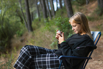 a teenage girl in casual clothes sits on a chair in a Camping and looks at the phone, 