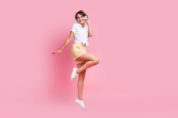 Foto op Canvas Full length photo of carefree nice young gorgeous lady touch her wireless blue headphones dancing in air isolated on pink color background © deagreez