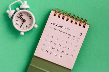 Desk calendar for February 2024 and clock on a green background.