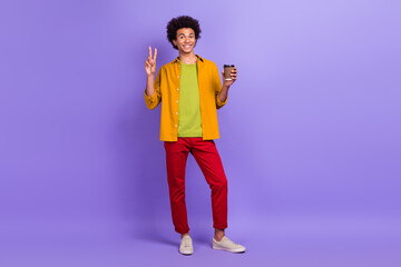 Photo of cheerful nice positive man wear stylish clothes walk drink espresso hand v-sign cappuccino isolated on purple color background