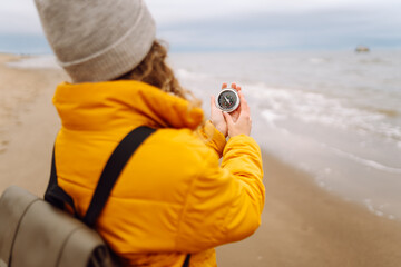 Woman traveler looking for directions with a compass on the beach by the sea. Active lifestyle. Adventure concept.