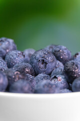 Macro photography of fresh antioxidant natural blueberries in a white bowl. Close-up of ripe blueberries on a green background. Concept of healthy eating. Vertical photo, water drops