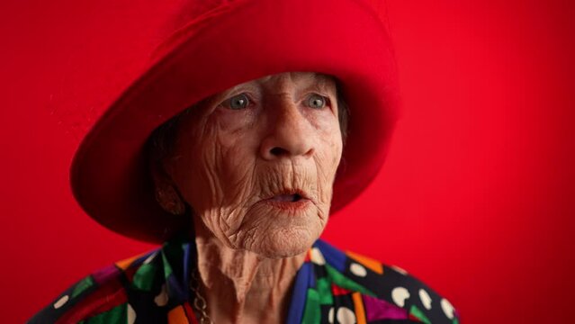 Slow motion saying WOW, a happy fisheye caricature of funny elderly woman with red hat isolated on red background.