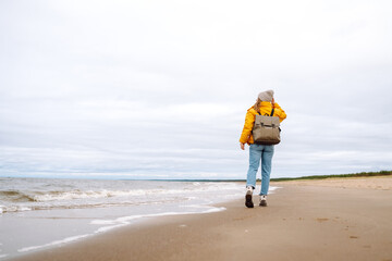Attractive woman on a windy cold beach. A beautiful tourist woman in stylish clothes enjoys life by the sea. Travel, nature concept.
