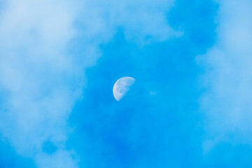 waning moon between clouds over the blue sky