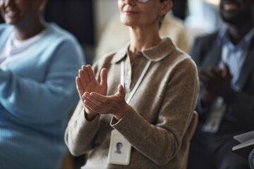 Hands of mature businesswoman in beige woolen pullover applauding to speaker at conference or seminar while sitting in front of camera