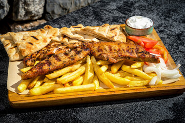 Close-Up photo of perfectly grilled meat, golden French fries, soft pita bread, and a medley of fresh vegetables artfully arranged on a rustic wooden board.  