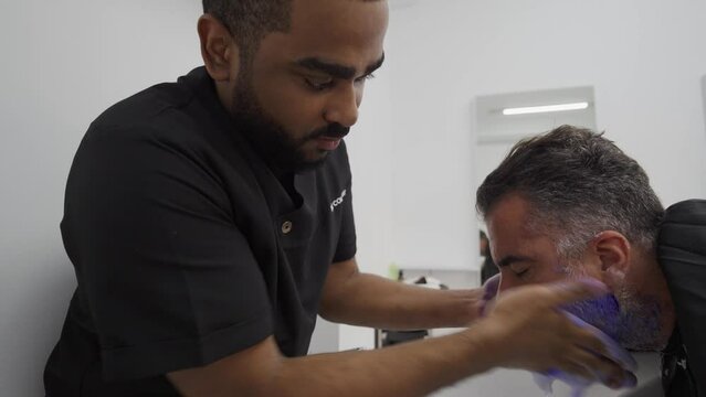 Afro-Latino barber applying antiyellow shampoo to client beard during dye.MOV