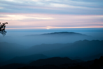 Golden sunset illuminates mountains, clouds, and a tranquil forest, casting a warm orange embrace over the serene landscape