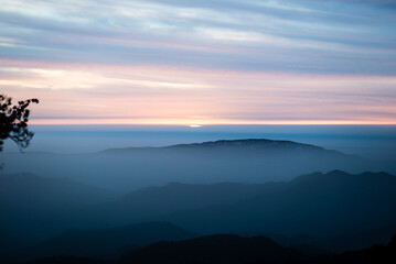 Golden sunset illuminates mountains, clouds, and a tranquil forest, casting a warm orange embrace over the serene landscape.
