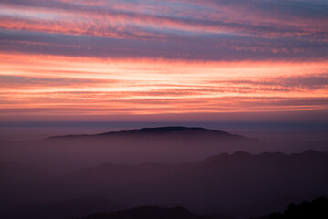 Golden sunset illuminates mountains, clouds, and a tranquil forest, casting a warm orange embrace over the serene landscape.